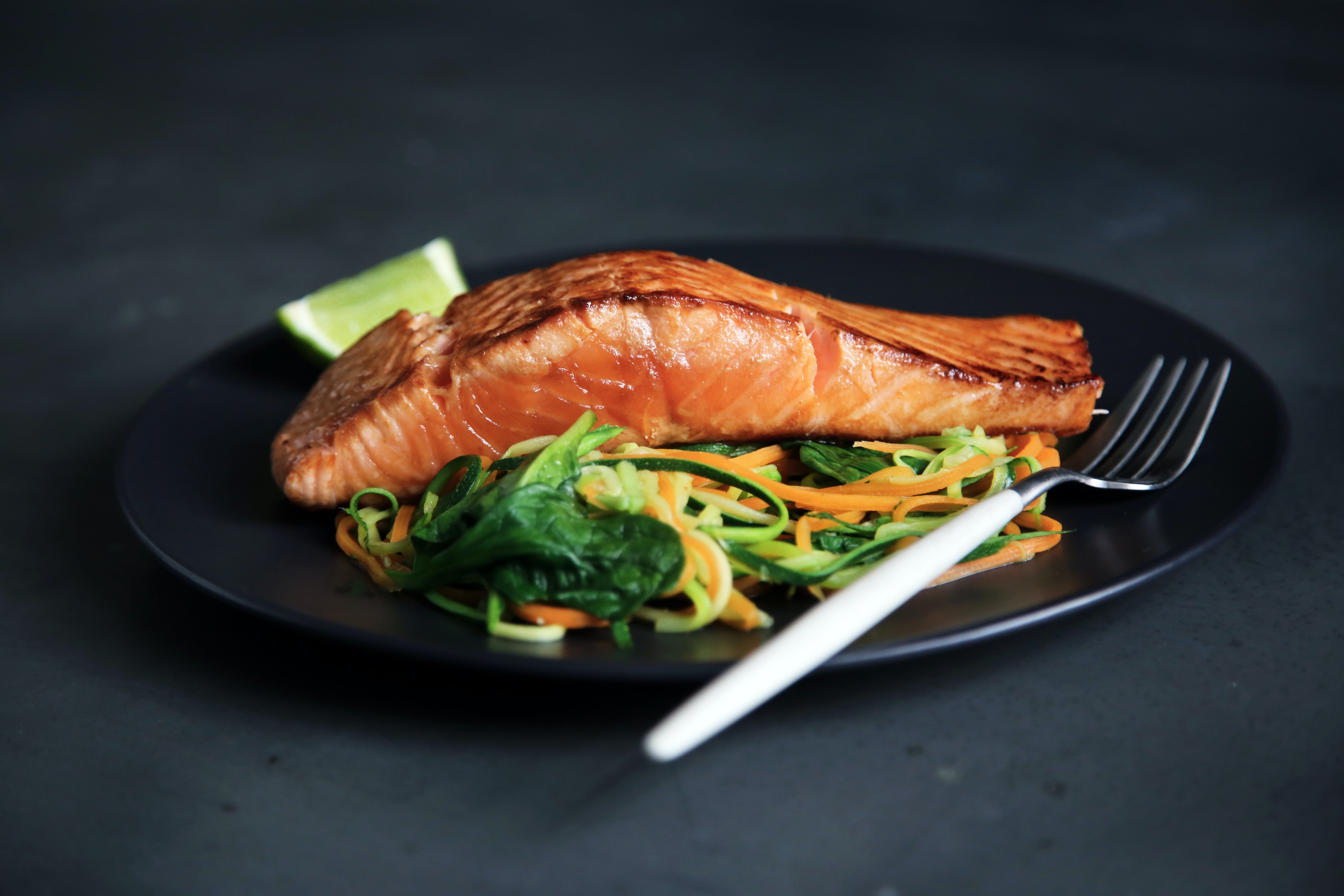 A plated meal with a salmon filet, salad, and lime wedge.